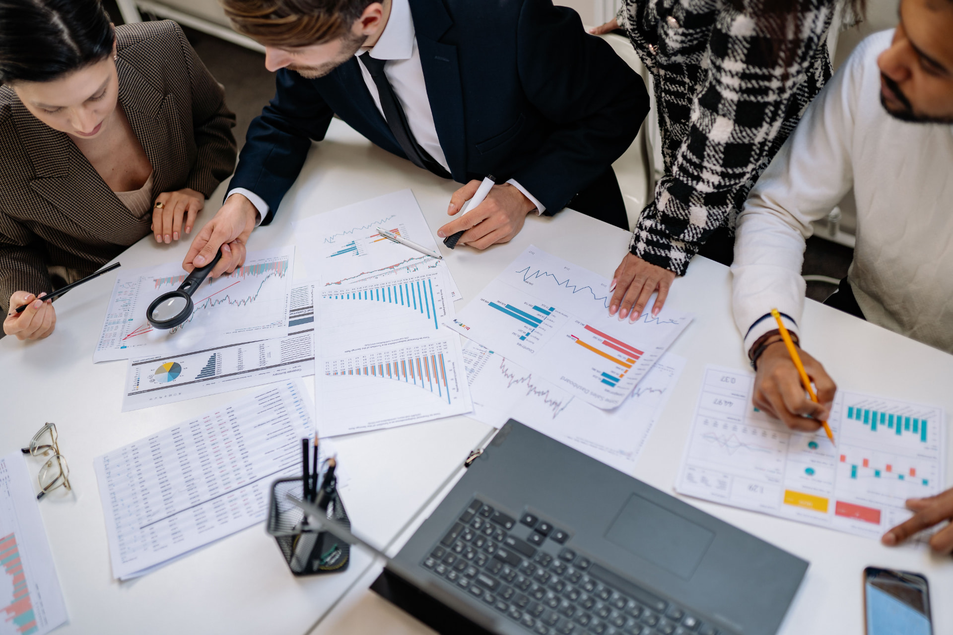 Overhead view of a finance team reviewing printed charts and financial reports around a table with a laptop