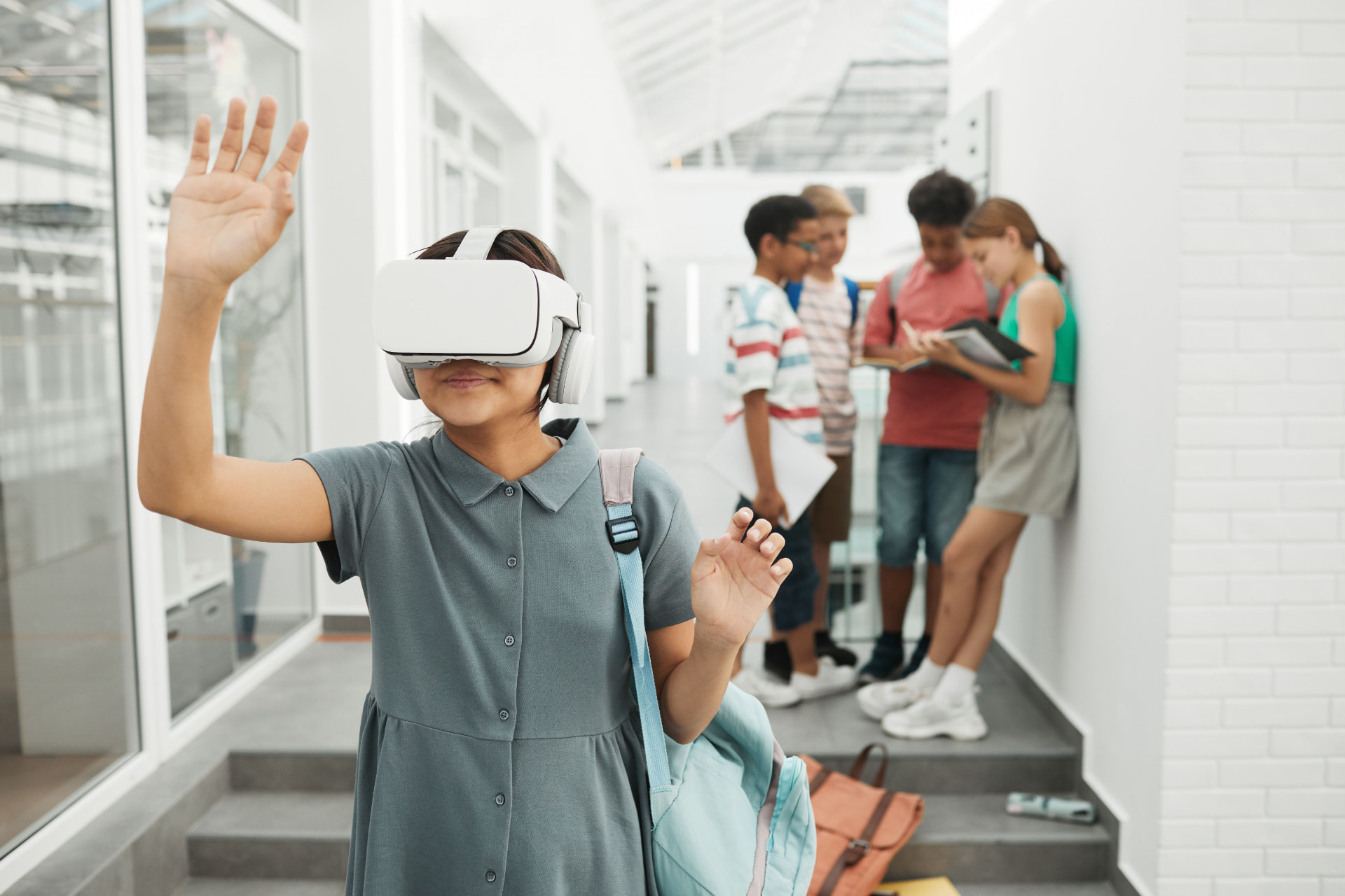 Student wearing a white VR headset in a school hallway while classmates talk at the top of a staircase