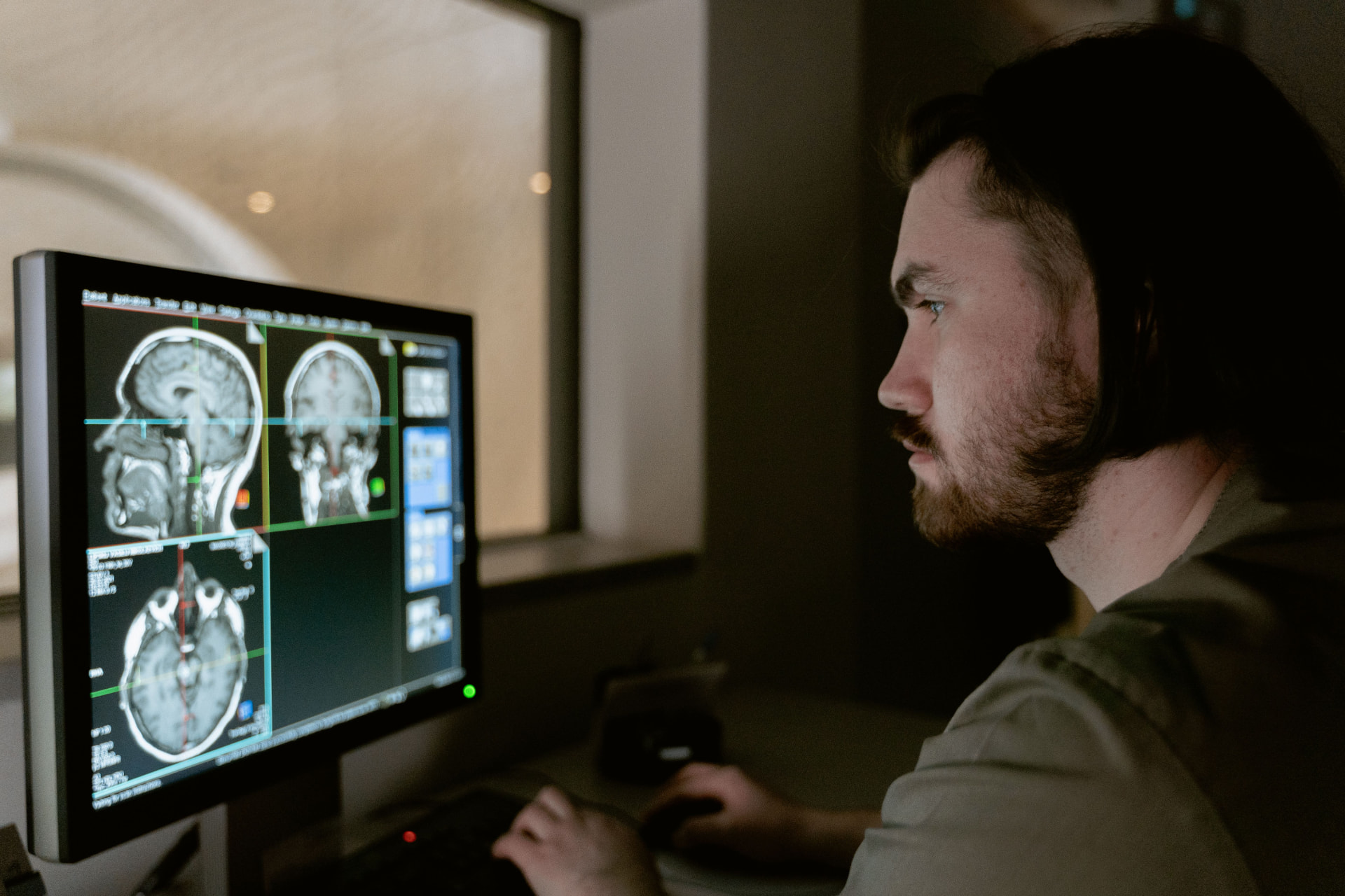 Medical professional seated at a diagnostic monitor reviewing brain scans in a dim imaging control room